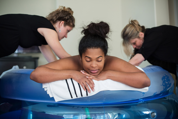 A birthing person is supported by DONA doulas in a blue water tub